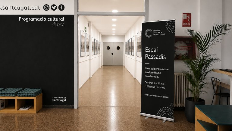 Entrada de l'Espai Passadís dels Centres Culturals de Sant Cugat, amb un passadís convertit en espai expositiu de fotografia, un roll-up informatiu i una planta decorativa a l'entrada