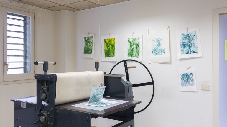 Tòrcul de gravat en primer terme i una exposició d'estampes penjades a la paret d'un taller de gravat contemporani.