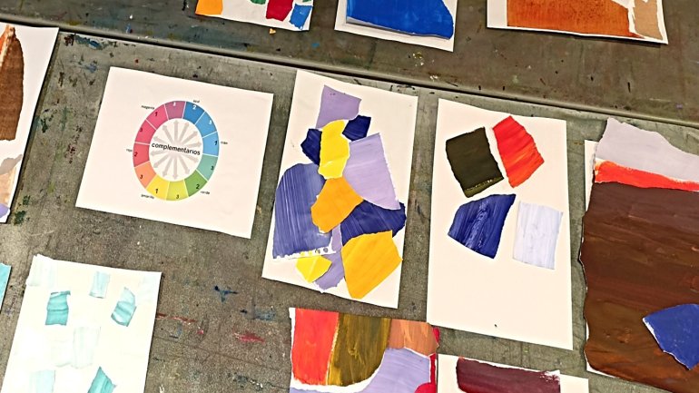 Fulls amb exercicis d’estampació i composicions de color disposats sobre una taula de treball durant un taller d’experimentació artística.