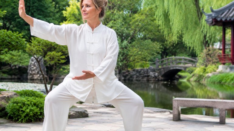 Dona practicant tai-txi en un jardí, amb vestimenta tradicional blanca i una postura d'equilibri, transmetent calma.