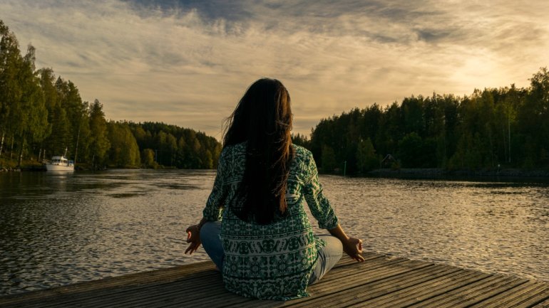 Persona practicant meditació davant d'un llac, en un entorn natural que transmet calma, presència i connexió interior.