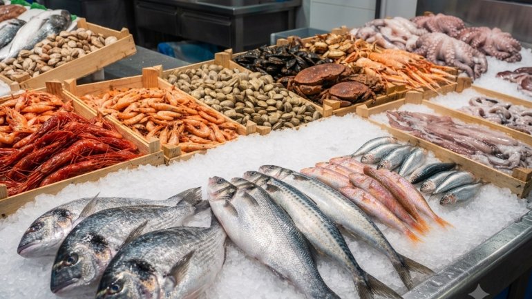 Aquesta imatge mostra una exposició detallada de peix i marisc fresc en una peixateria, presentats sobre una base de gel picat i en caixes de fusta rústiques.
En primer pla, directament sobre el gel, destaca una selecció de peix fresc alineat:
* Peixos 