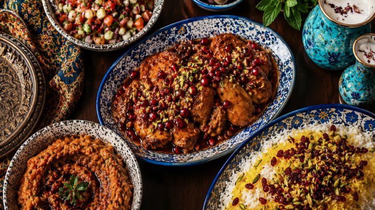 Sí. La imatge mostra una taula parada amb un conjunt de plats que recorden molt la cuina persa (iraniana) o, més àmpliament, la gastronomia de l'Orient Mitjà. La presentació és molt acurada, amb vaixella decorada en tons blaus i blancs i una estètica eleg