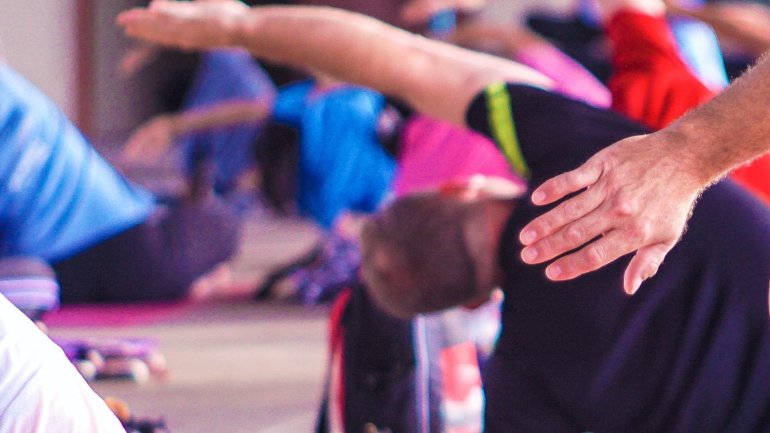 Grup de persones fent pilates estirant esquena i braços 