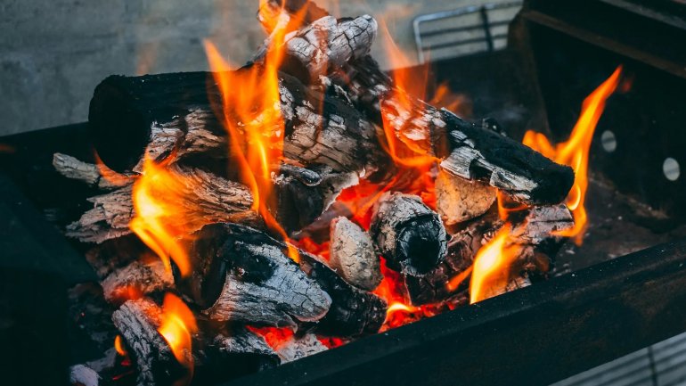 Brases de carbó enceses amb flames vives dins d'una barbacoa, preparades per cuinar a la graella.