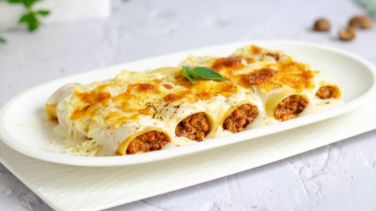 Canelons de carn gratinats amb beixamel i formatge, servits en una safata blanca.
