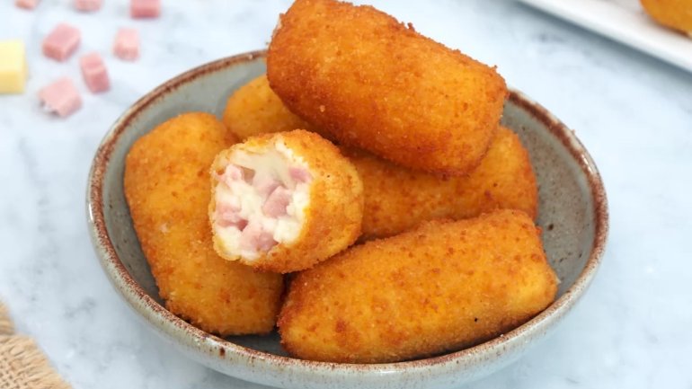 Bol amb croquetes de pernil i beixamel daurades i cruixents, una d'elles oberta per mostrar el farcit cremós.