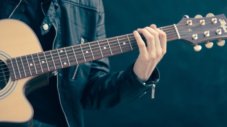 Una persona sosté una guitarra acústica mentre col·loca els dits sobre el mànec per formar un acord. La imatge mostra l'instrument en primer pla. 