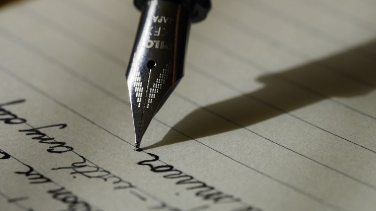 Primer pla d’una ploma estilogràfica escrivint sobre un full de paper amb línies, representant l’escriptura, la creativitat i l’aprenentatge.