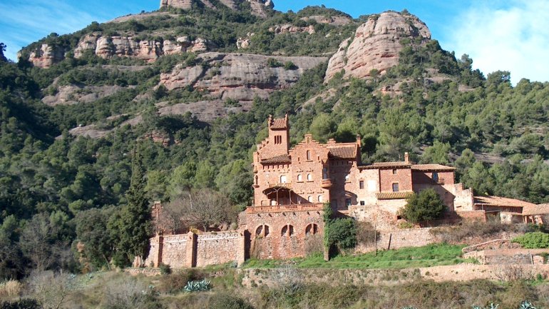 El Marquet de les Roques, casal d'estil historicista neoromànic, de pedra vermella situat al peu d'una muntanya de conglomerat, envoltada de boscos mediterranis i vegetació, sota un cel blau i en un entorn natural característic del Vallès Occidental.