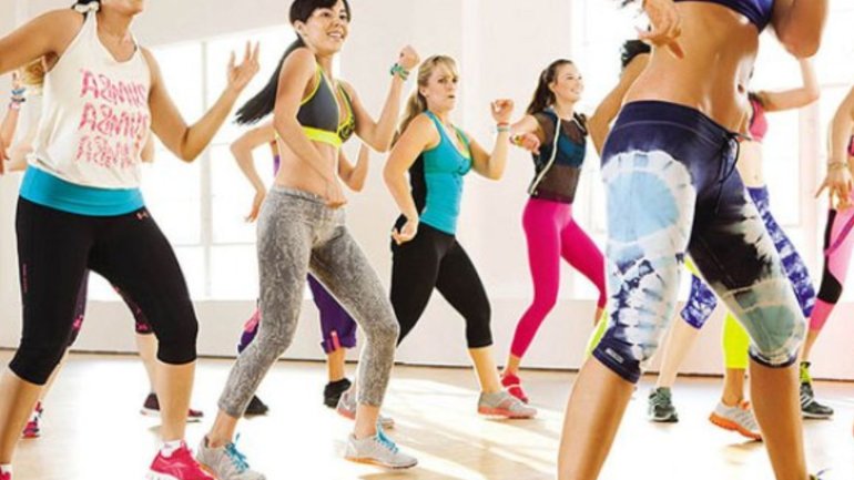 Participants fent una classe de zumba en grup en un estudi de dansa, amb moviments enèrgics i roba esportiva