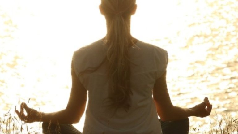 Persona asseguda en posició de meditació a l'aire lliure, amb les cames creuades i les mans en gest de relaxació, davant d'un llac il·luminat per la llum del sol