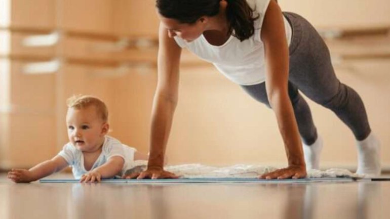 Persona practicant gimnàstica postpart amb un nadó al costat en una sala d'activitats