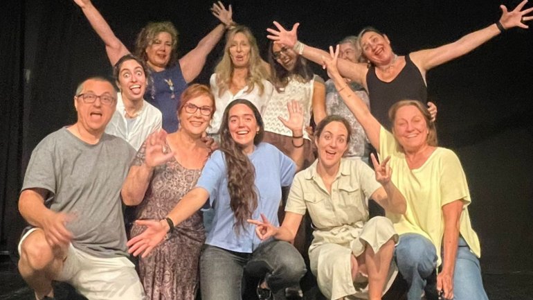 Grup de participants d’un taller d’expressió i gestió de les emocions posant junts sobre un escenari, amb gestos expressius i actitud alegre en un ambient teatral.