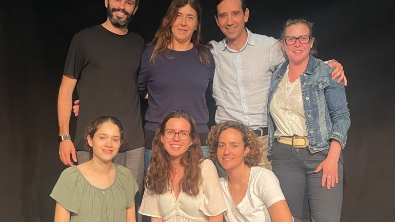 Grup de persones participants en un curs per aprendre a parlar en públic, fotografiades sobre un escenari i davant d’un fons negre, amb actitud propera i somrient.