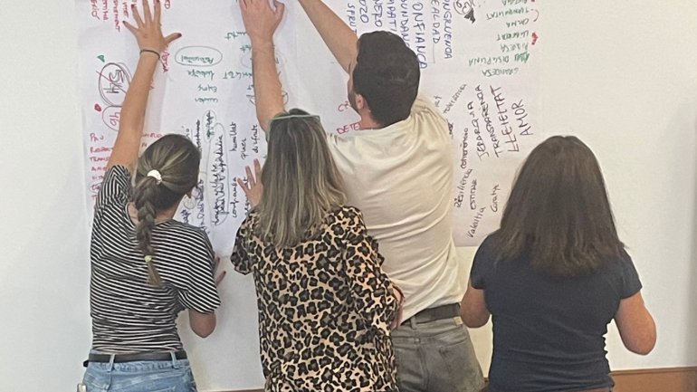 Quatre persones participant en una activitat de PNL, col·laborant davant d’un mural ple de paraules, idees i anotacions escrites amb diferents colors.